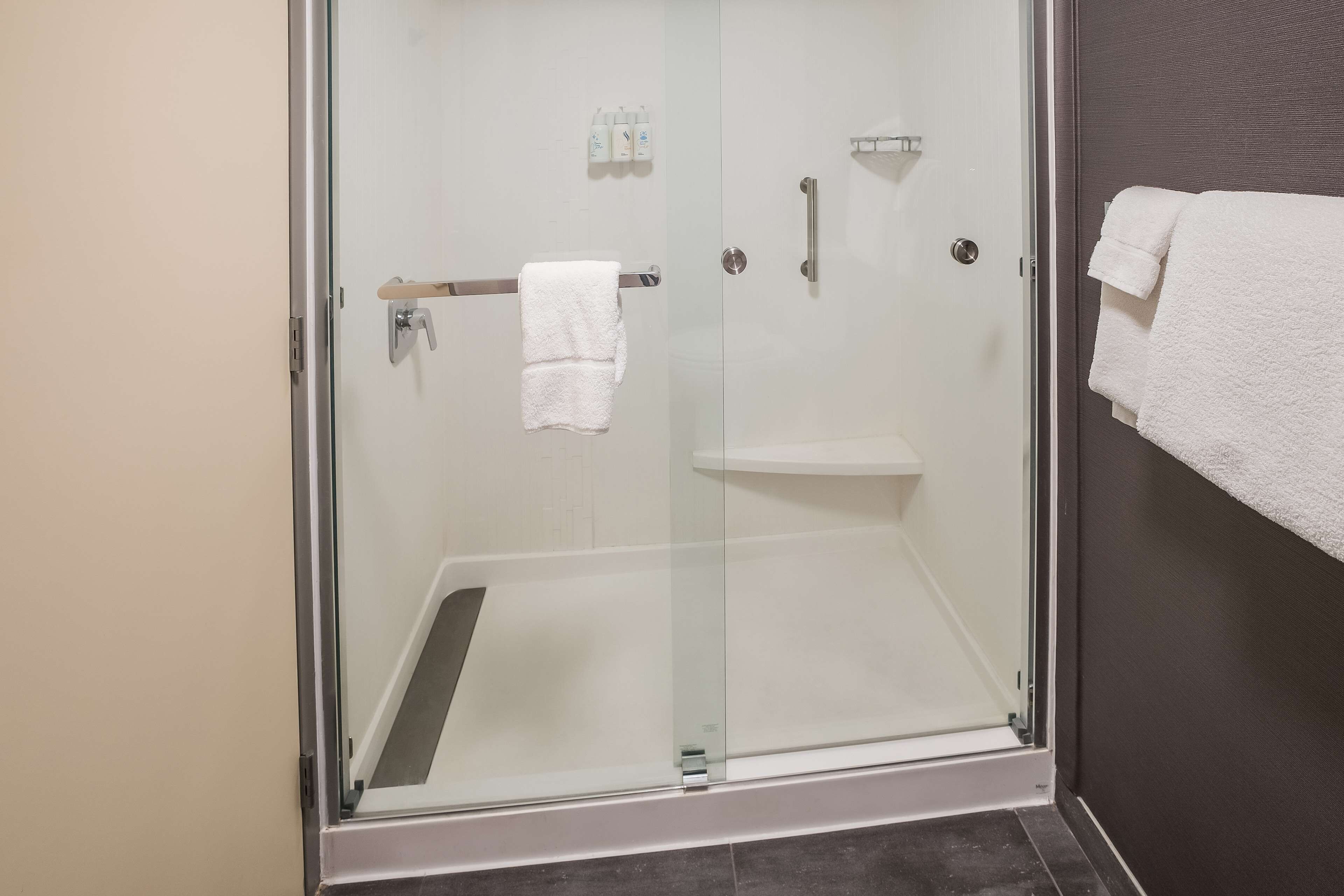 Une cabine de douche fermée par des parois en verre, avec une serviette blanche accrochée à la poignée de la porte et une autre serviette blanche accrochée au mur.