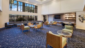 A spacious lobby with a large seating area, multiple tables, and a TV screen on the wall. - Sonesta Select Phoenix Chandler (Chandler)