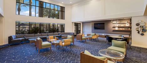 A spacious lobby with a large seating area, multiple tables, and a TV screen on the wall.