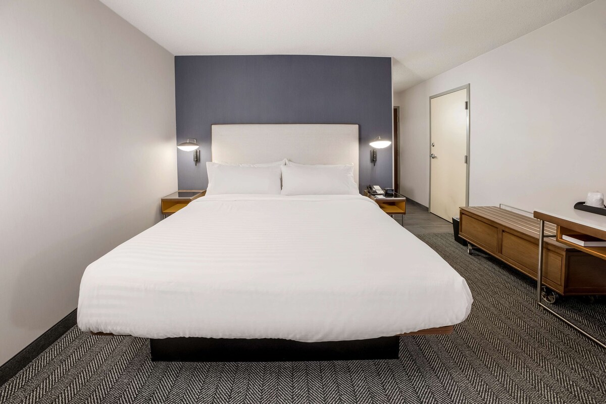 Una habitación de hotel con una cama grande, mesitas de noche, un escritorio y un armario.