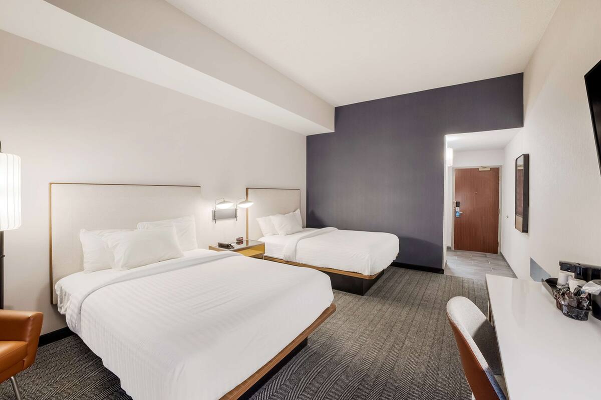A hotel room with two beds, a desk, and a chair.