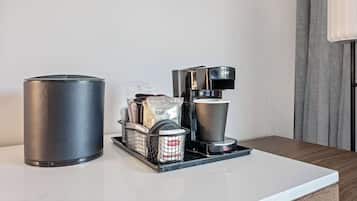 A coffee station with a coffee maker, a cup, a basket with coffee pods, and a container.