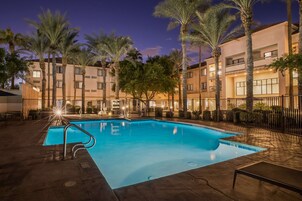 A swimming pool surrounded by palm trees and a multi-story building with balconies.