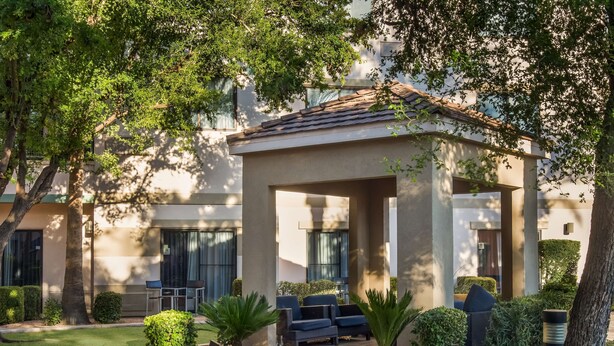 A covered outdoor seating area with chairs and tables, surrounded by well-maintained landscaping and trees. - Sonesta Select Phoenix Chandler (Chandler)