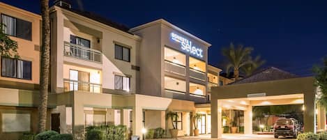 A hotel with a modern design, featuring a prominent 'Bonesta Select' sign, a covered entrance, and a parking area with a vehicle.
