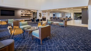 A spacious lobby with multiple seating areas, a flat-screen TV mounted on the wall, and a large window providing a view of the outside. - Sonesta Select Phoenix Chandler (Chandler)