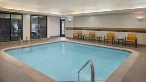 A swimming pool with a tiled border, a metal ladder, and several chairs with cushions.