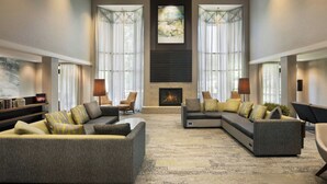 A spacious living room with a fireplace, large windows, and modern furniture. - Courtyard by Marriott Springfield Airport (Springfield)
