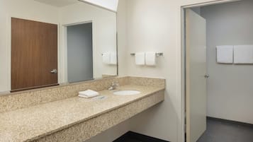 A bathroom with a granite countertop, a sink, a mirror, and a door leading to another room.