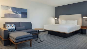 Una habitación de hotel con una cama grande, un sofá, una mesita y una obra de arte colgada en la pared.