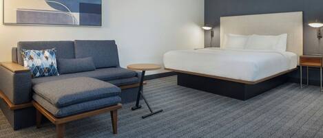 A hotel room with a large bed, a sofa, a small table, and a wall-mounted artwork.