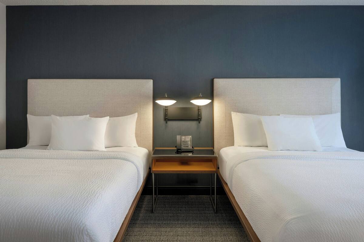 A hotel room with two beds, a nightstand with a telephone, and wall-mounted lamps.