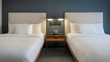 A hotel room with two beds, a nightstand with a telephone, and wall-mounted lamps.