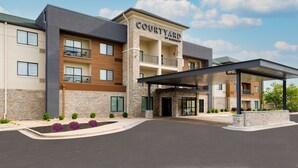 A multi-story hotel with a stone facade, a covered entrance, and a balcony on the second floor. - Courtyard by Marriott Springfield Airport (Springfield)