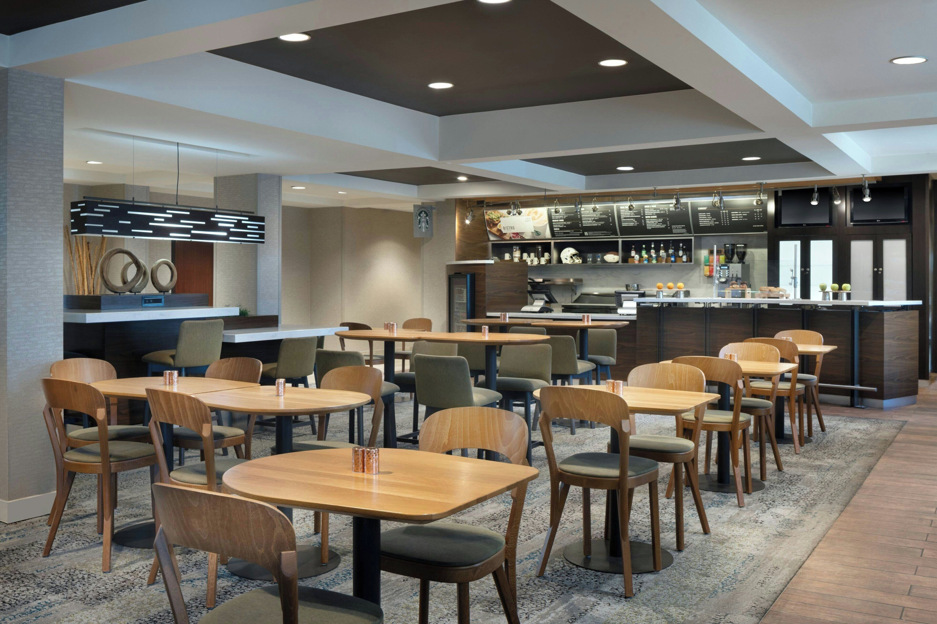 A modern restaurant with wooden tables and chairs, a bar area, and a menu display.