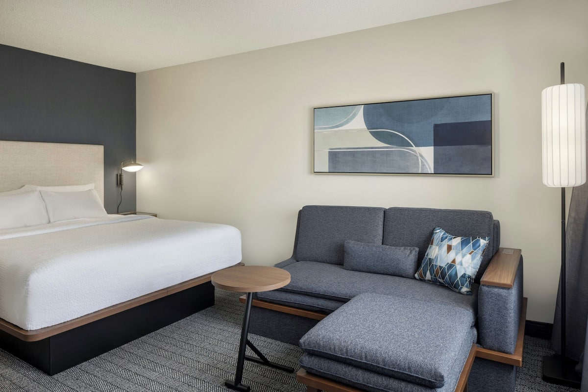 A hotel room with a bed, a sofa, a small table, and a lamp.