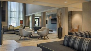 A modern living room with a sectional sofa, armchairs, a coffee table, and a TV mounted on the wall. - Courtyard by Marriott Springfield Airport (Springfield)