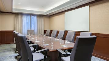 A conference room with a long table, multiple chairs, and a projector screen.