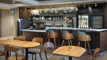 Un área de bar moderna con mobiliario de madera, una máquina de café y una pizarra de menú.