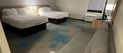 A hotel room with two beds, a sofa, a patterned carpet, and a window with blinds.