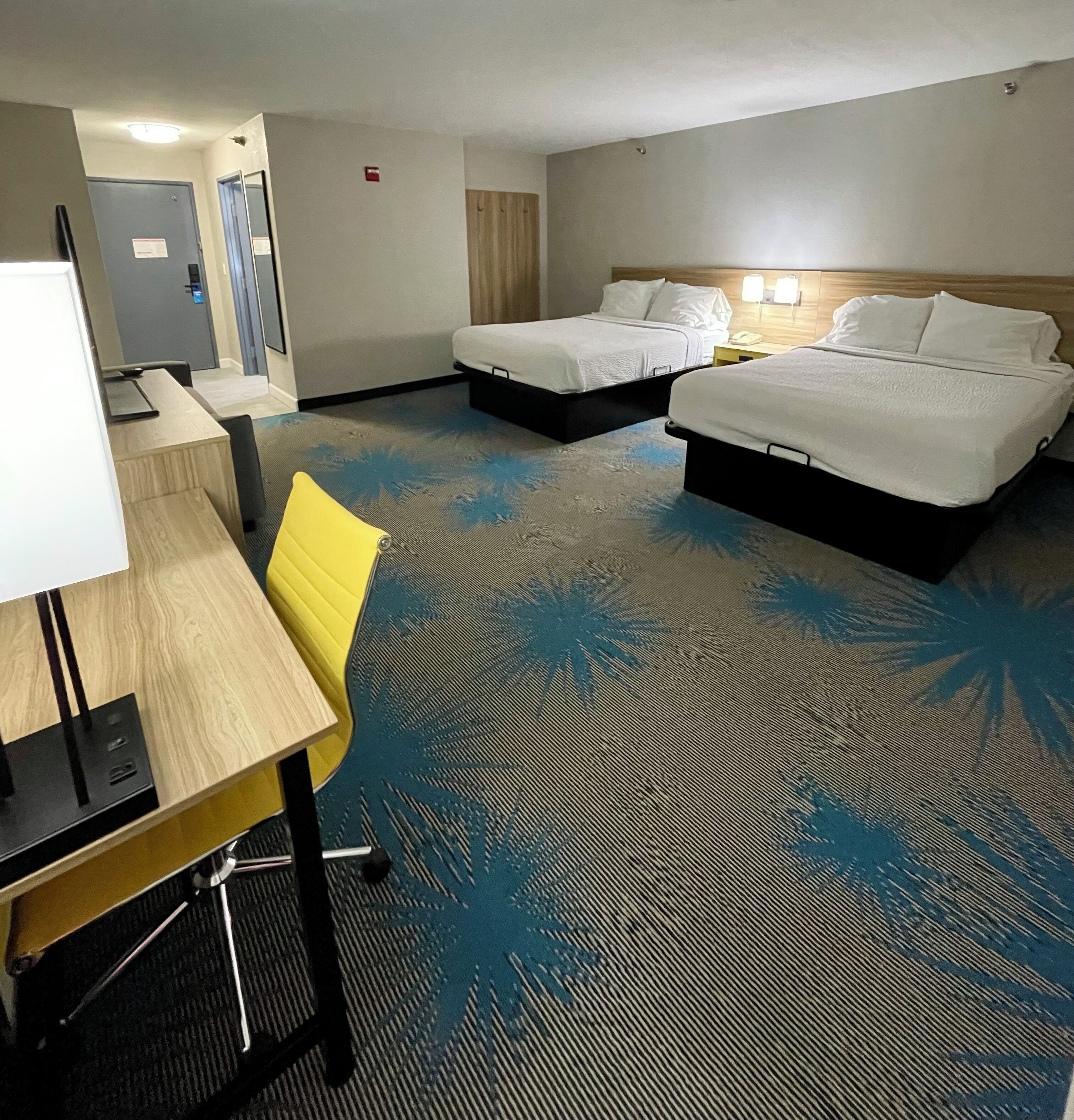Une chambre d’hôtel avec deux lits, un bureau, une chaise et une moquette à motifs de feuilles de palmier.