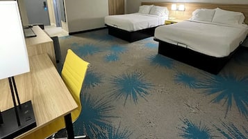 A hotel room with two beds, a desk, a chair, and a carpet with a palm leaf pattern.