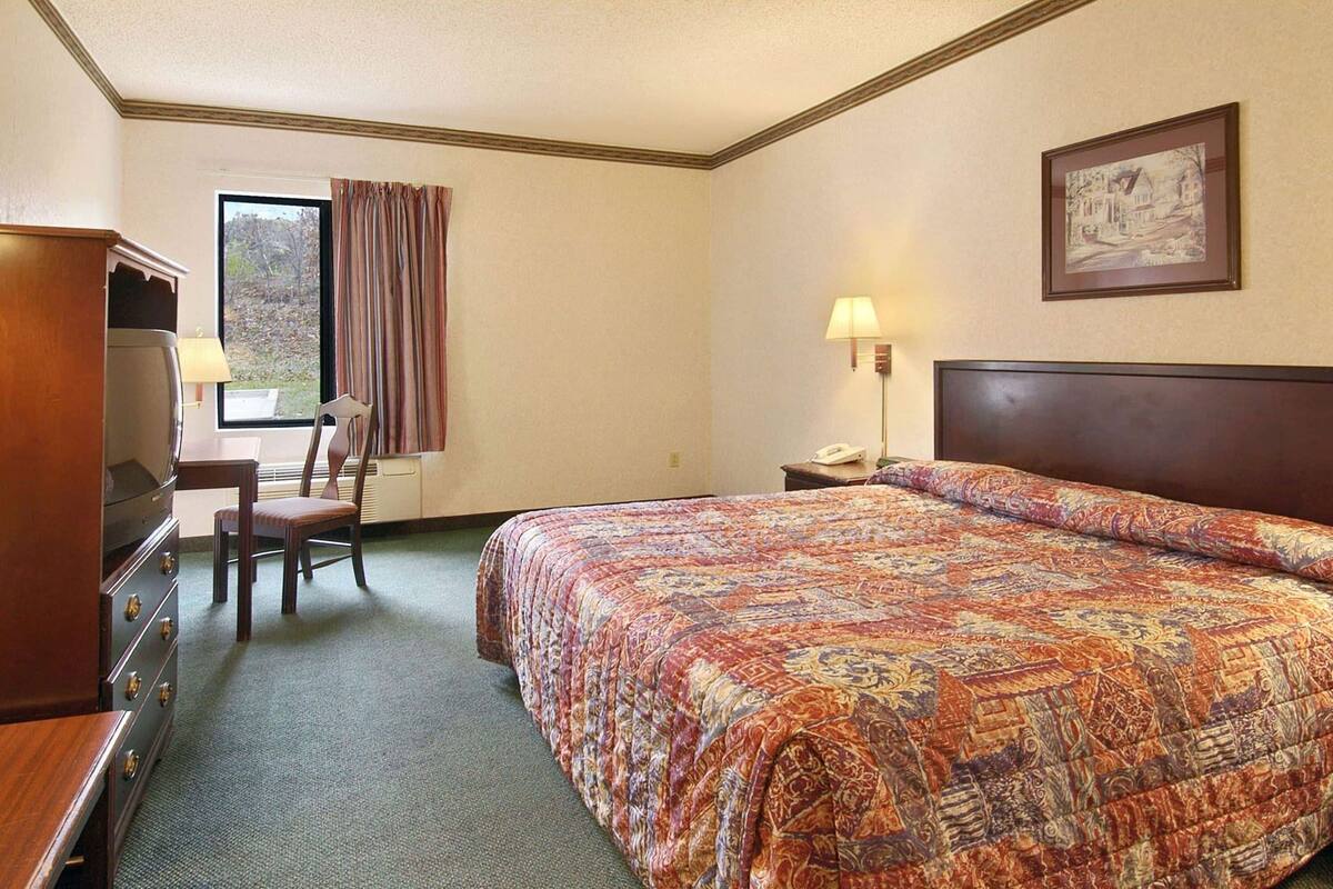 Ein Hotelzimmer mit Bett, Schreibtisch, Stuhl, Lampe und einem Gemälde an der Wand.