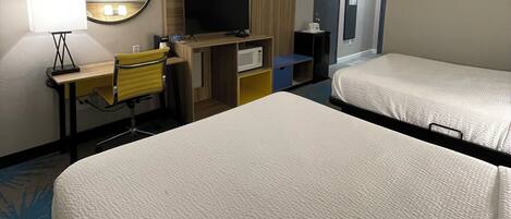 A hotel room with two beds, a desk with a chair, a television, a microwave, and a mirror.