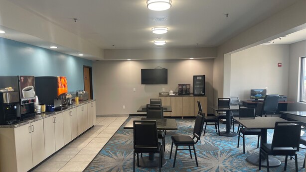 Un área de cocina moderna con estación de café, televisor de pantalla plana y zona de estar con mesas y sillas.