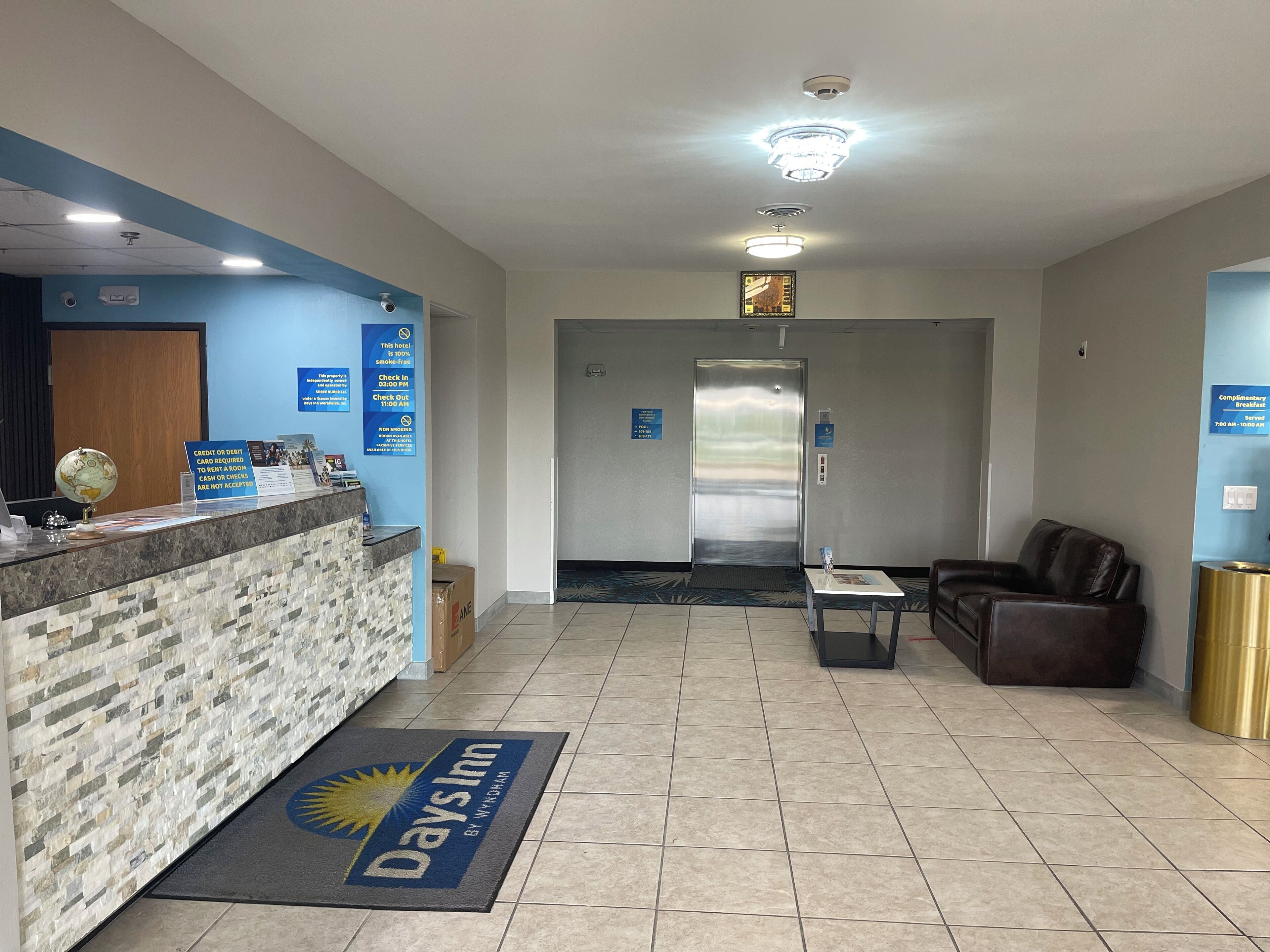 A hotel reception area with a reception desk, a check-in counter, a seating area with a leather couch, and an elevator.