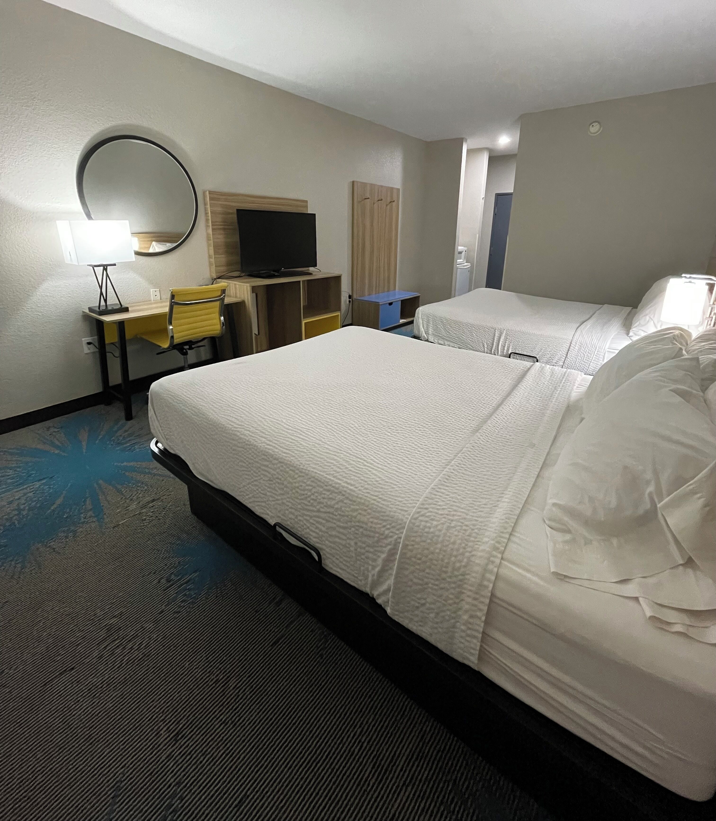 A hotel room with two beds, a desk with a chair, a television, and a mirror.