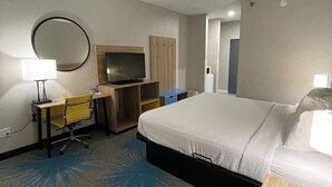 Una habitación de hotel con cama, escritorio y silla, televisión, armario y espejo.