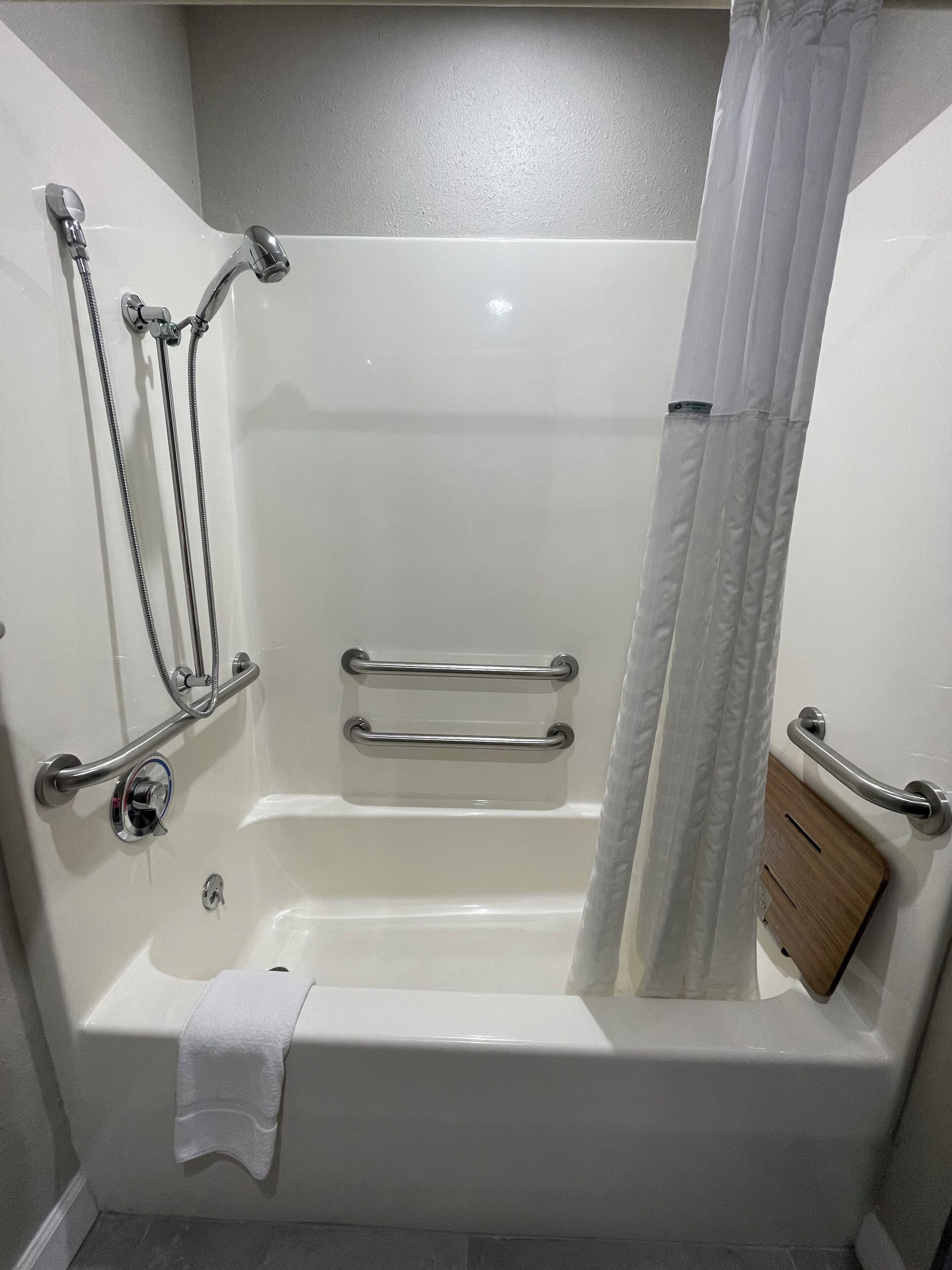 A modern bathroom with a walk-in shower, grab bars, and a wooden panel.