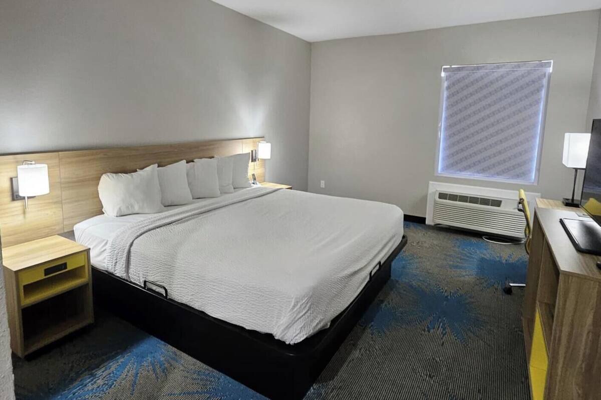 Ein Hotelzimmer mit einem Galaxy Z Fold5 Bett, einem Schreibtisch mit Computer und einem Fenster mit Jalousien.