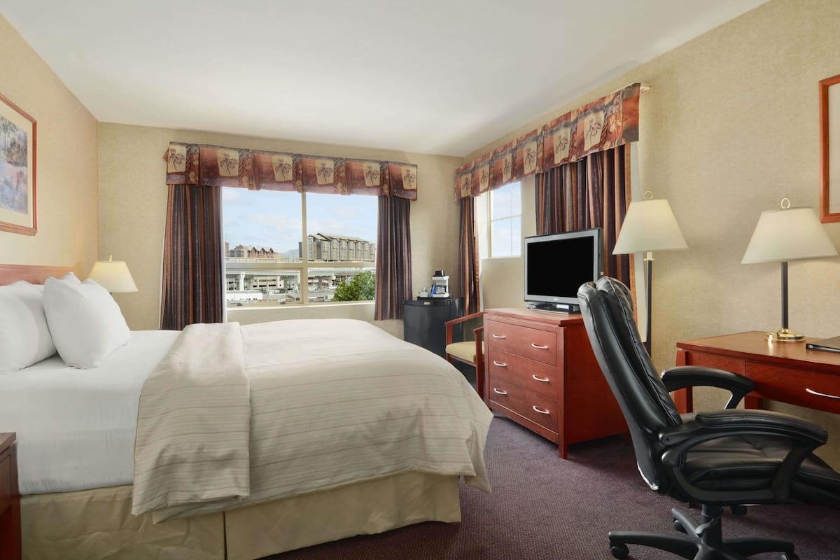 A hotel room with a large bed, a desk with a computer, a chair, and a television.
