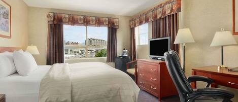 A hotel room with a large bed, a desk with a computer, a chair, and a television.