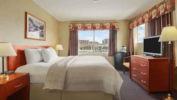 Quarto de hotel com cama grande, televisão, escrivaninha com gavetas, luminária e quadro na parede.