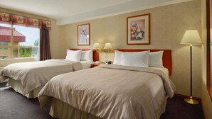 A hotel room with two beds, a nightstand with lamps, and framed artwork on the walls.