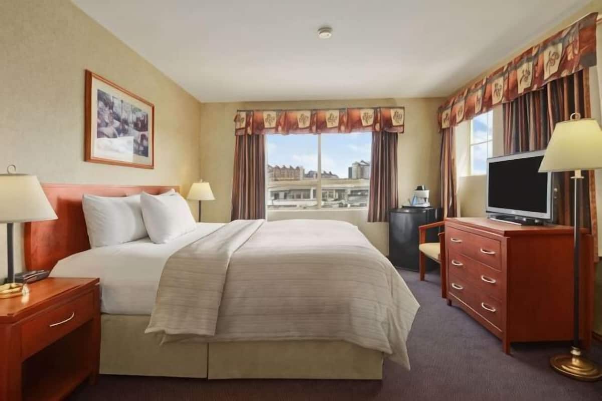 A hotel room with a bed, a television, a desk with drawers, a lamp, a picture on the wall, and a window with curtains.