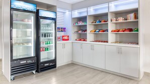 Une petite cuisine équipée de deux réfrigérateurs, d’étagères remplies d’en-cas et d’un four à micro-ondes.