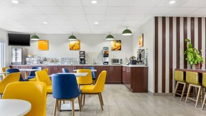 Un restaurant moderne avec des chaises jaunes et bleues, un comptoir avec des machines à café et un téléviseur fixé au mur.