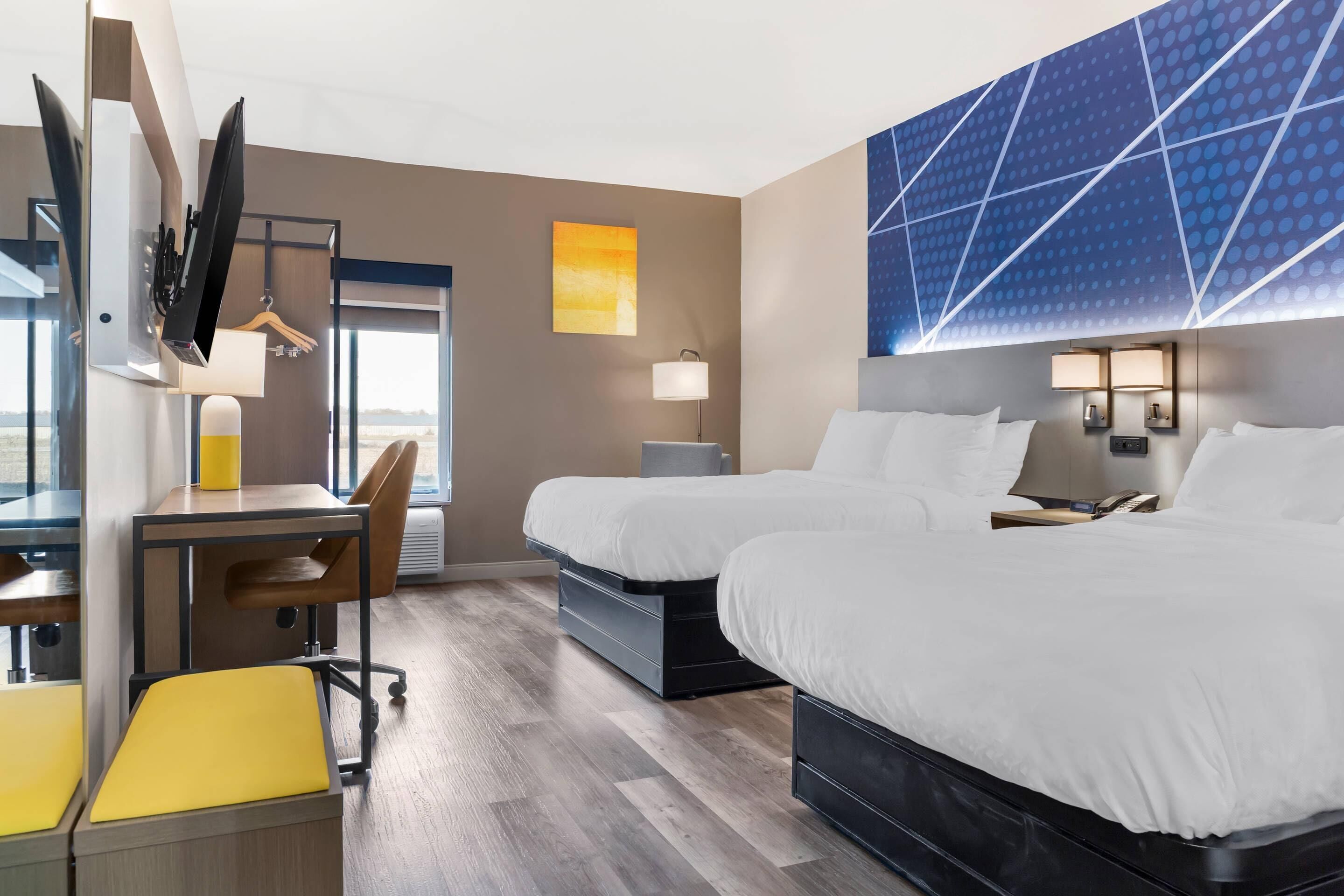 A hotel room with two beds, a desk, a chair, and a TV.