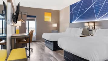 A hotel room with two beds, a desk, a chair, and a TV.