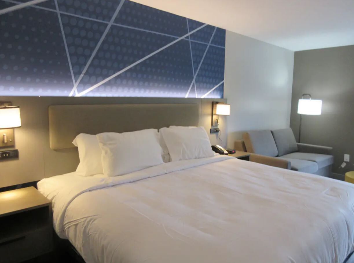 A hotel room with a large bed, two bedside tables, a sofa, and a wall-mounted light fixture.