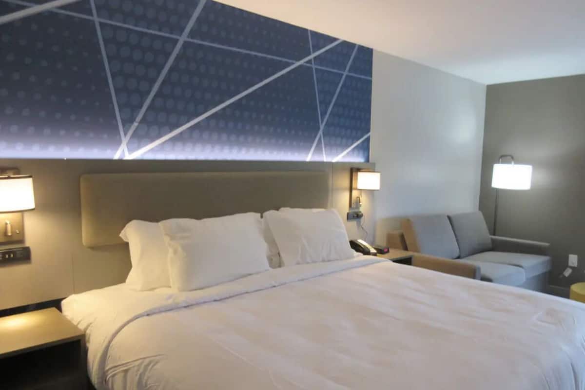 A hotel room with a large bed, two bedside tables, a sofa, and a wall-mounted light fixture.