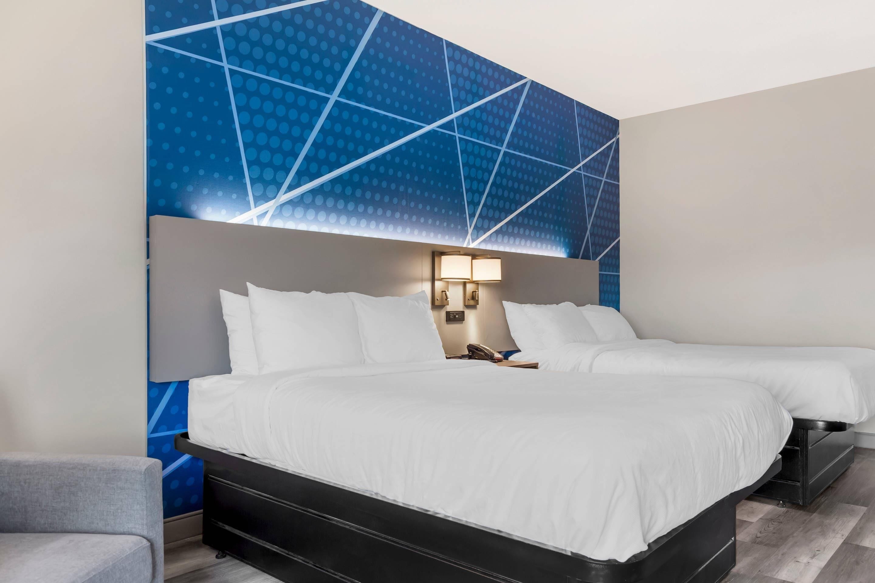 A hotel room with two beds, a nightstand, a lamp, and a blue patterned wall.