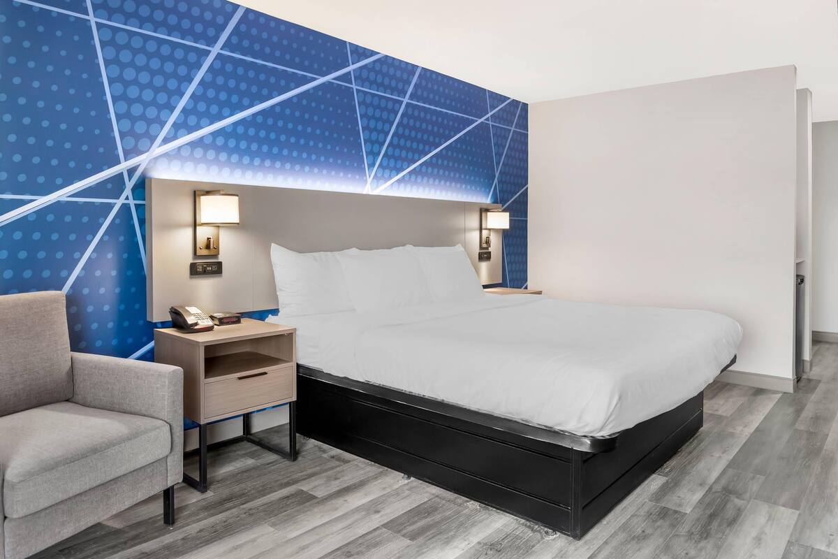 A hotel room with a bed, bedside tables, a chair, and a wall with a geometric pattern.