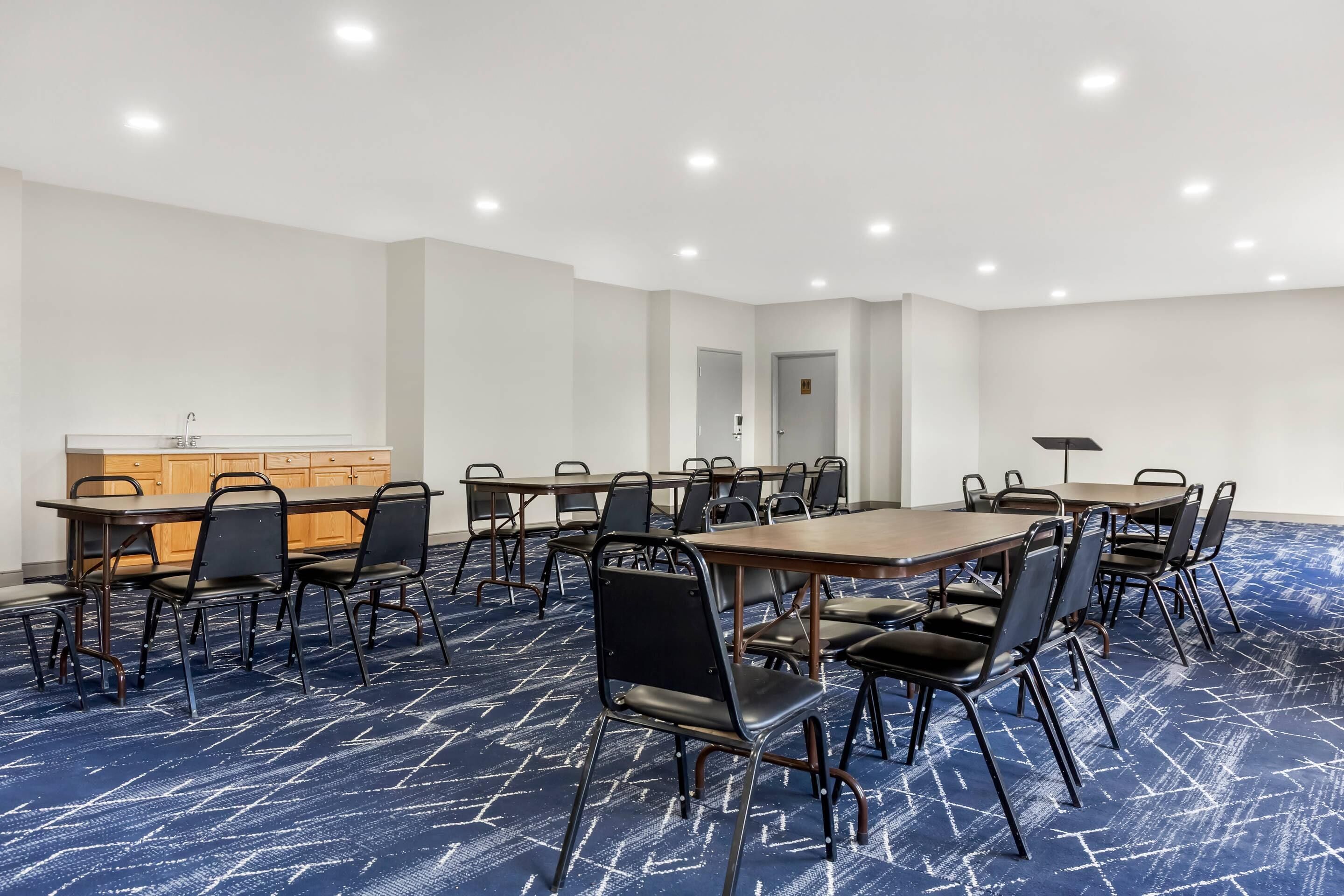 Une salle de conférence avec une longue table, des chaises, un petit coin cuisine et un sol recouvert de moquette.