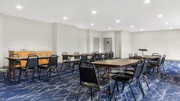 Une salle de conférence avec une longue table, des chaises, un petit coin cuisine et un sol recouvert de moquette.