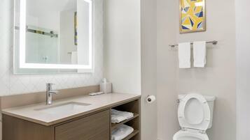 Une salle de bain équipée d’un lavabo, d’un miroir, d’un porte-serviettes, de toilettes et d’une œuvre d’art géométrique accrochée au mur.